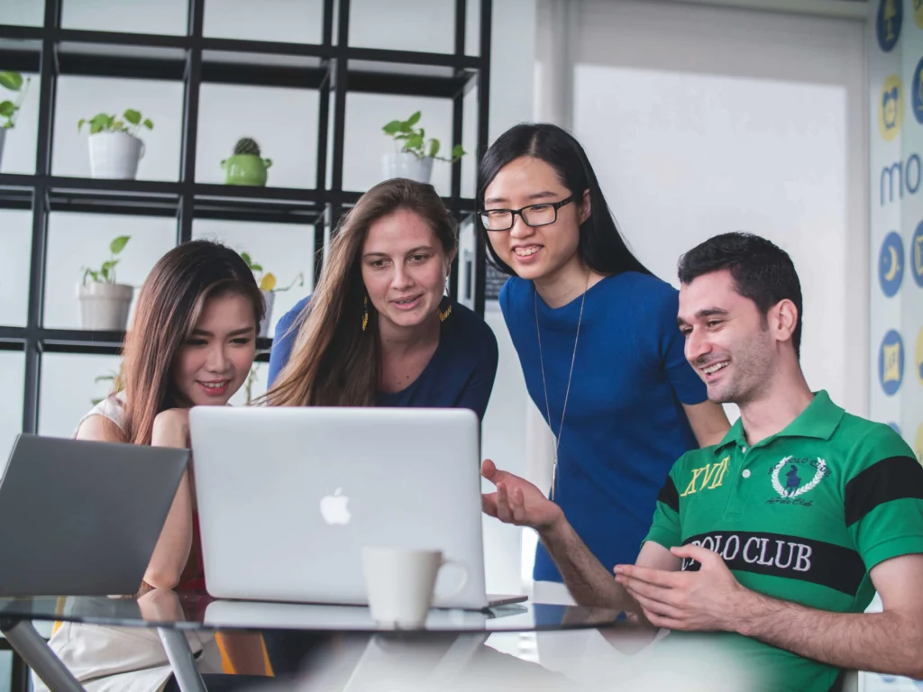 A modern office environment with a team of professionals celebrating a successful project, featuring a digital banner that reads 'Powerful Team Names For Work 2025.'